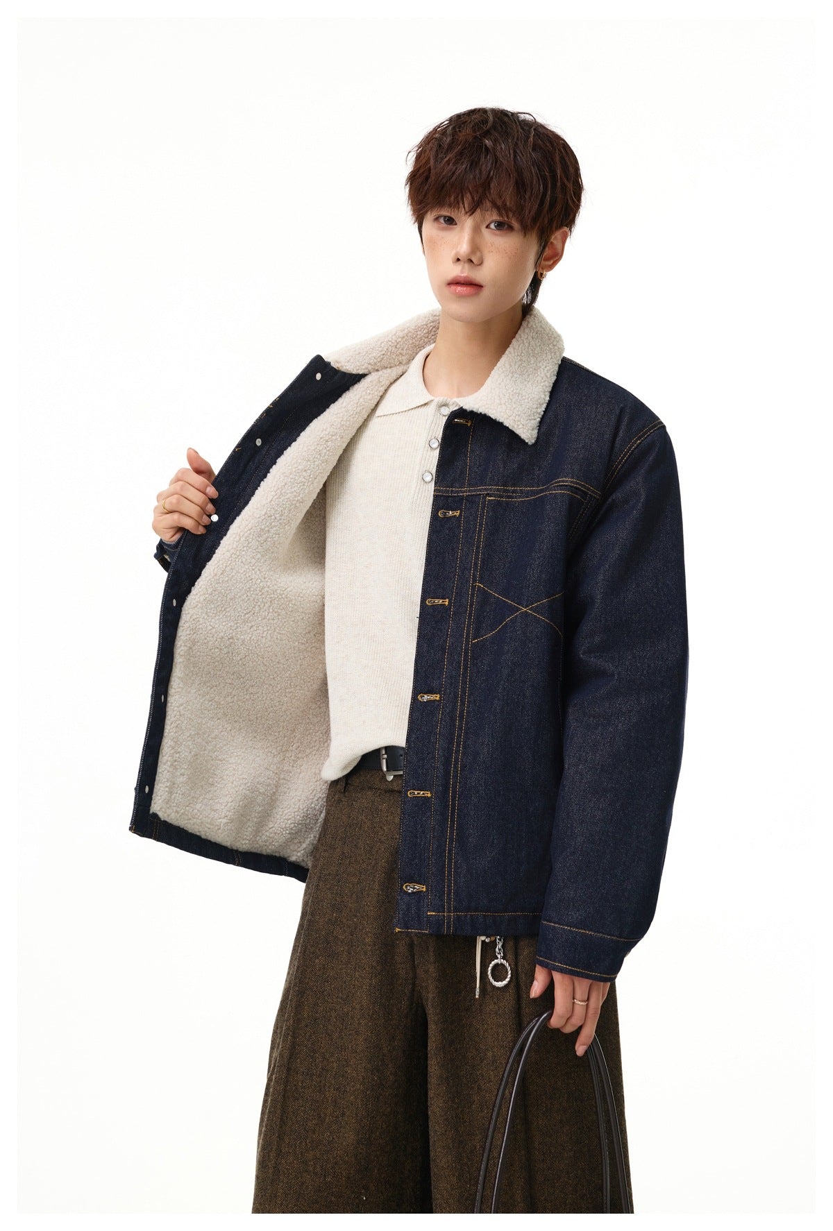 Model opening a dark indigo denim jacket to show its cream sherpa lining and collar.