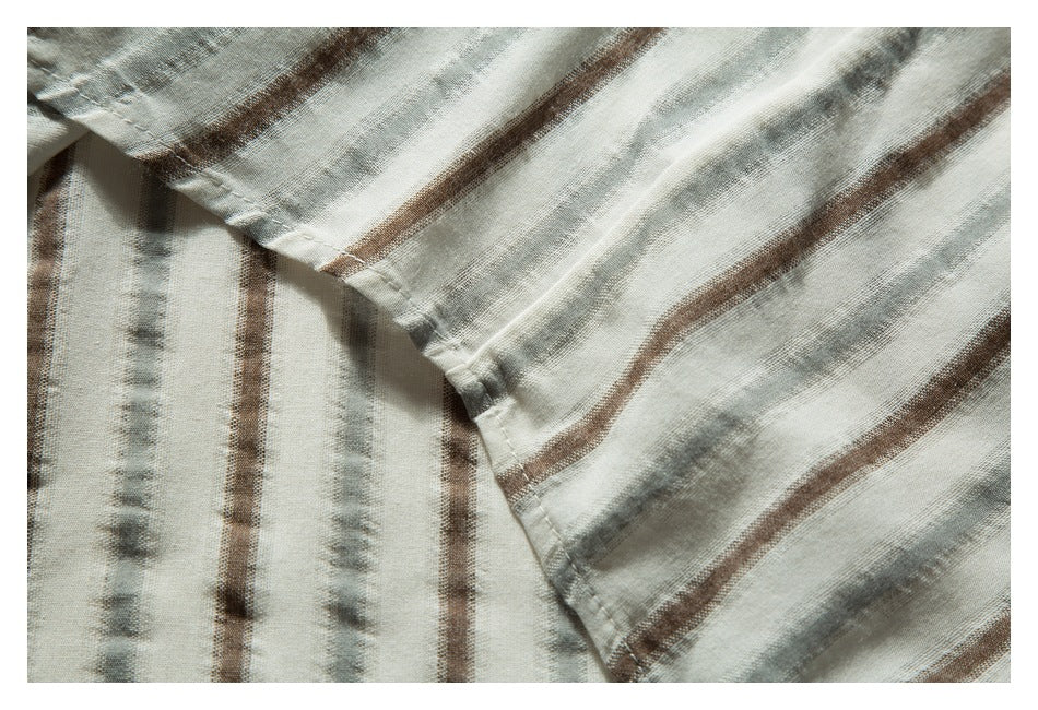 Close-up of overlapping off-white striped garment fabric with stitched edges and muted gray and brown stripes.