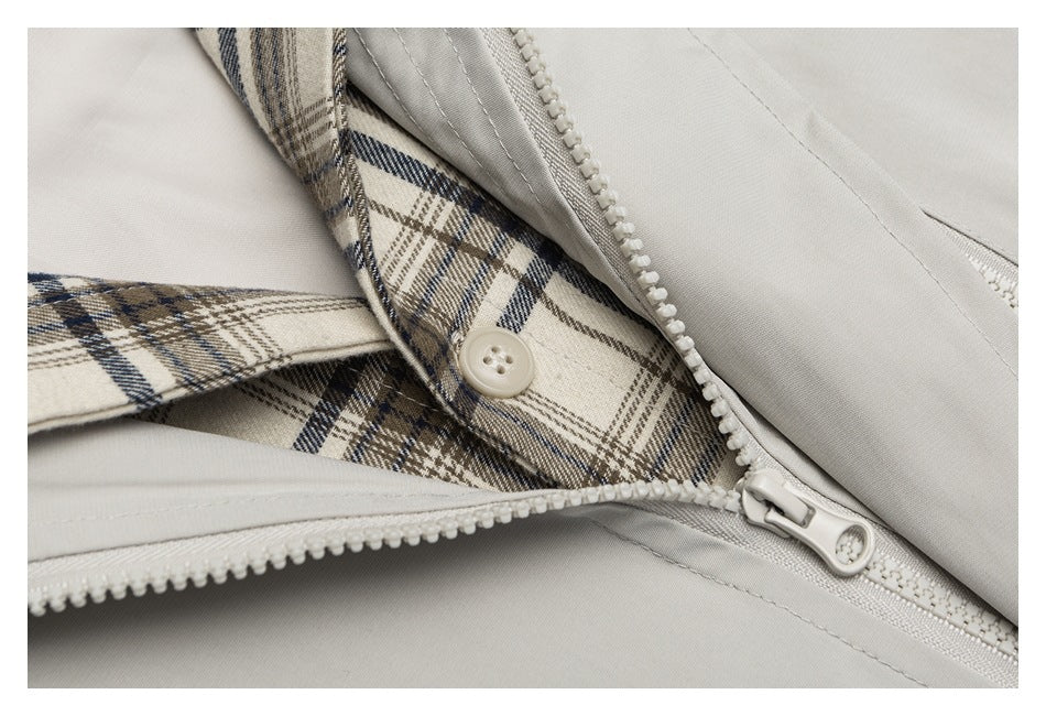 Close-up of a light gray garment partly unzipped, showing plaid lining and a button.