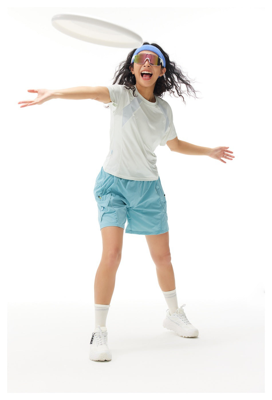Model playing with a flying disc in a white color-block T-shirt and turquoise shorts.