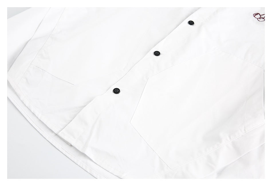 Close-up of a white shirt front with black buttons, angular patch pockets, and a small burgundy embroidered motif.