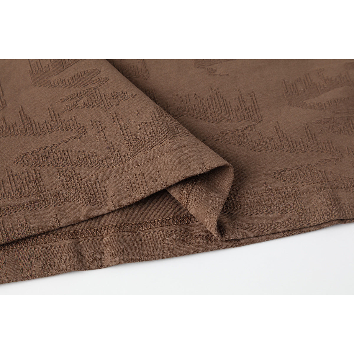 Close-up of the brown T-shirt's patterned fabric, folded sleeve, and stitched hem.