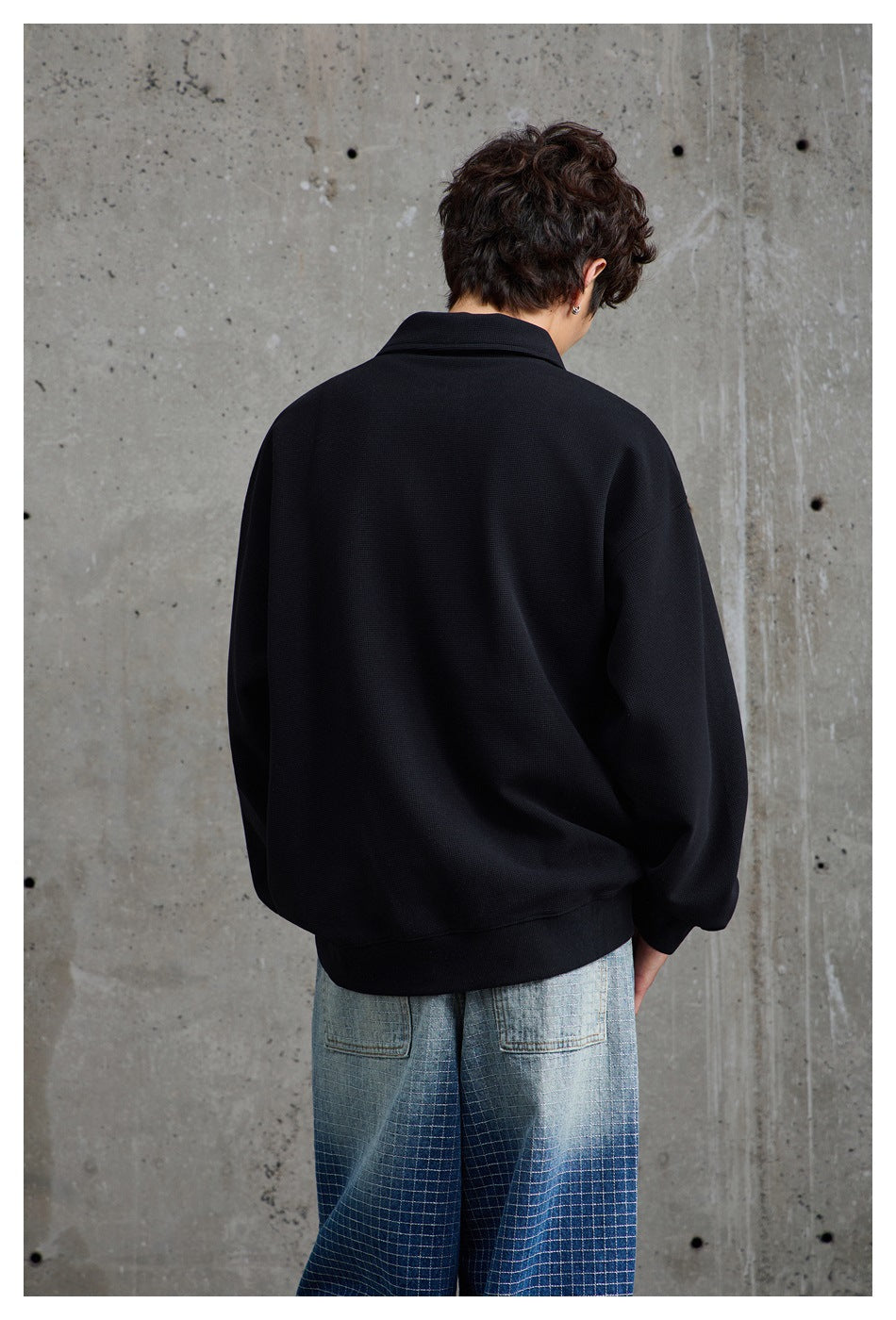 Rear view of a model wearing a black collared pullover and wide blue checked jeans.
