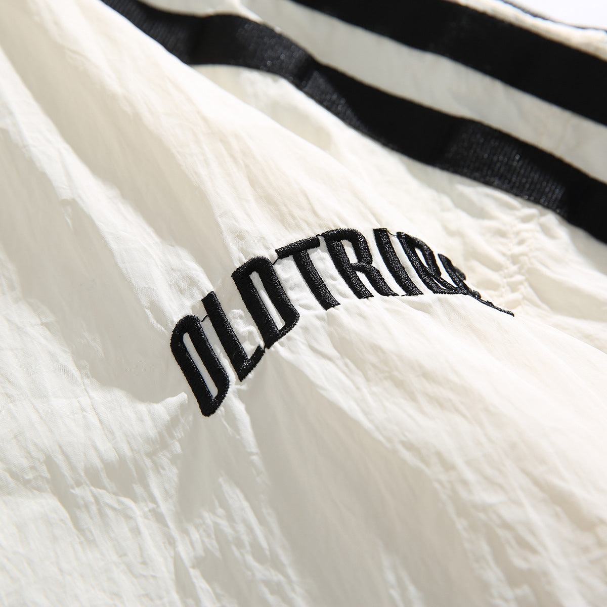 Close-up of black embroidered lettering on the crinkled ivory jacket, with a black stripe visible above.