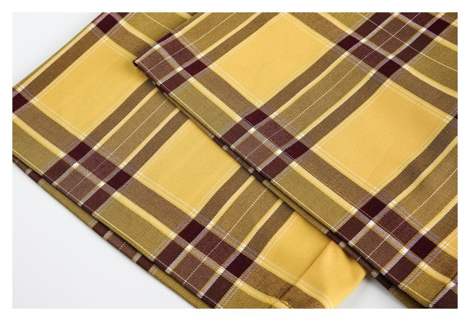 Close-up of folded mustard and brown plaid fabric with a visible stitched edge.