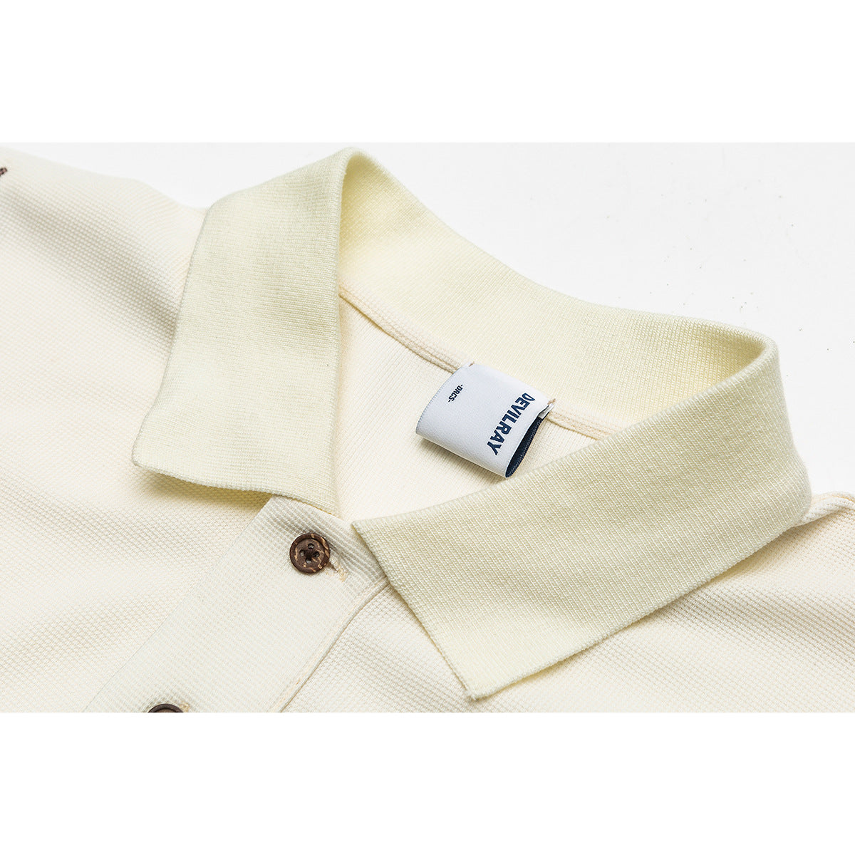 Close-up of an ivory collared shirt with brown buttons and a sewn neck label.