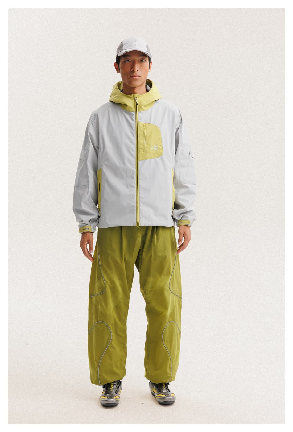 Full-length front view of a model wearing a light gray jacket with yellow-green accents and olive trousers.