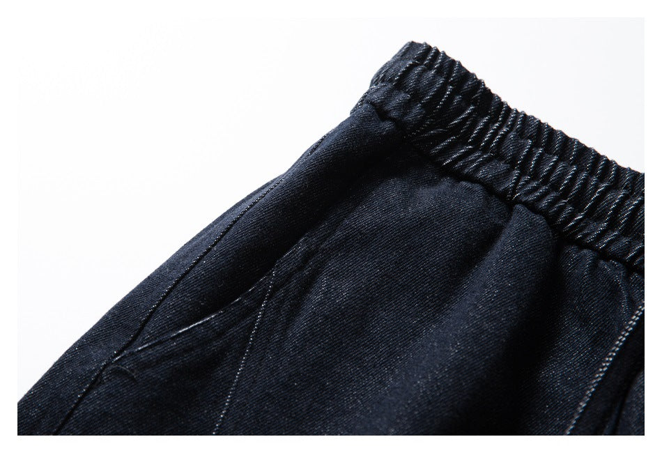 Close-up of a side pocket opening and elastic waistband on dark indigo pants.