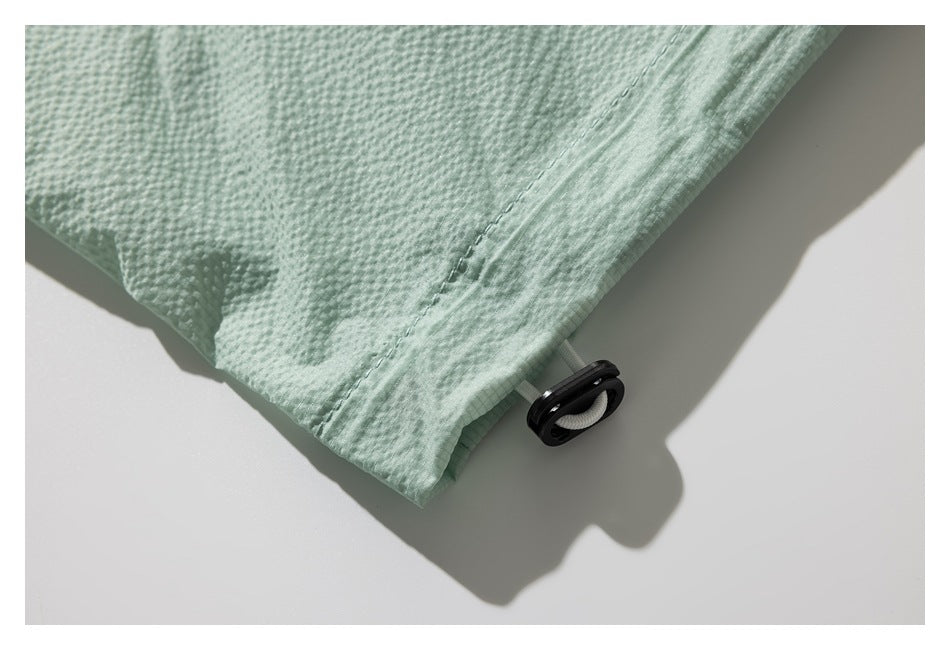 Close-up of the mint-green garment hem with a black cord lock and white drawcord.