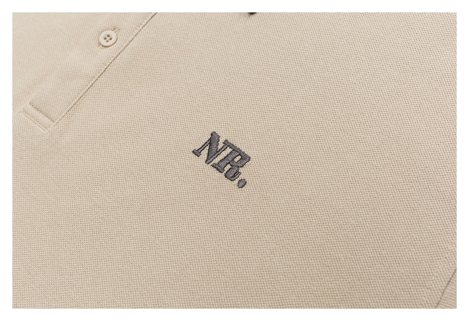 Close-up of dark NB embroidery on the chest of a beige textured polo shirt.