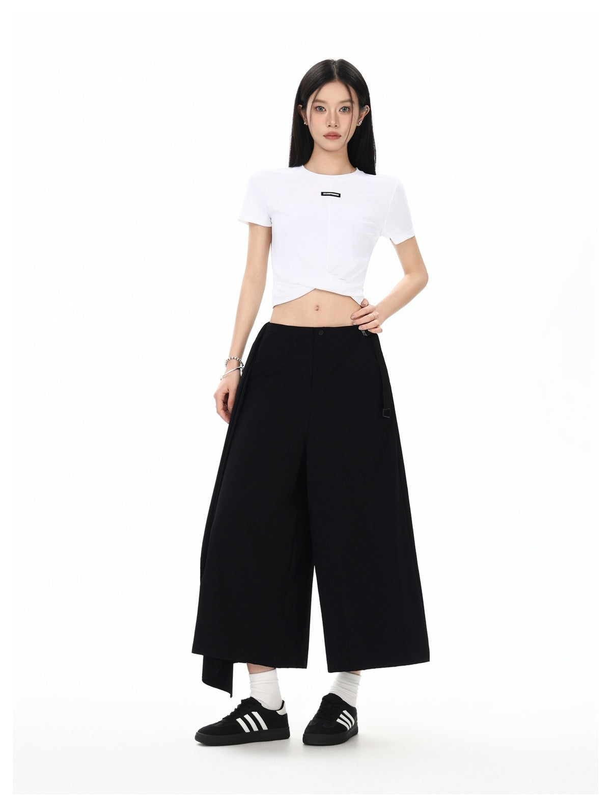 Full-length model wearing black wide-leg cropped trousers with an asymmetrical wrap panel and a white cropped T-shirt.