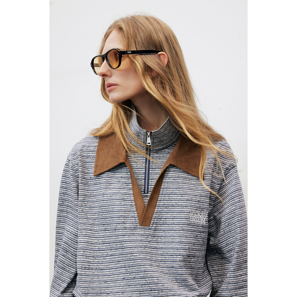 Woman wearing a gray and navy striped pullover with a brown contrast collar, V-shaped placket and zip neck.
