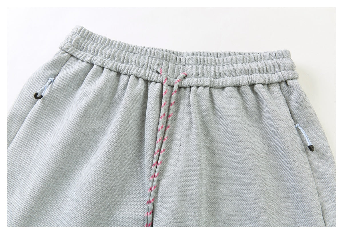 Close-up of the elastic waistband, pink-accented drawstring, and zippered pockets on light gray pants.