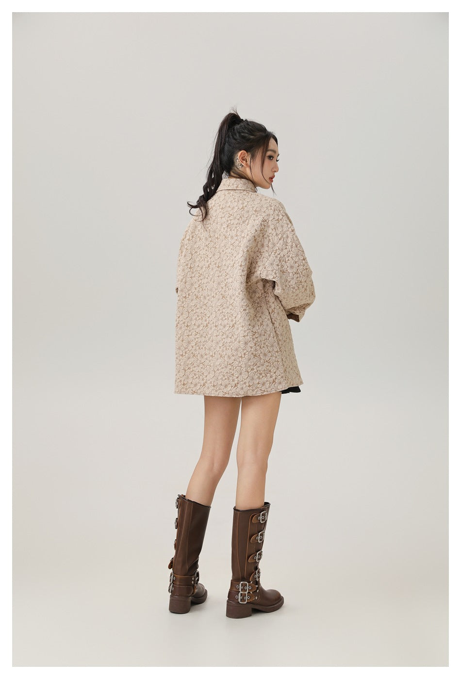 Rear view of a model wearing an oversized beige floral jacket and brown knee-high boots.