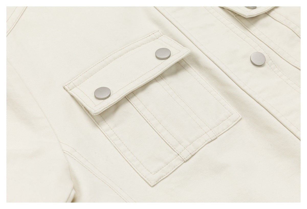 Close-up of an ivory jacket's stitched flap chest pocket with two metal snap buttons.
