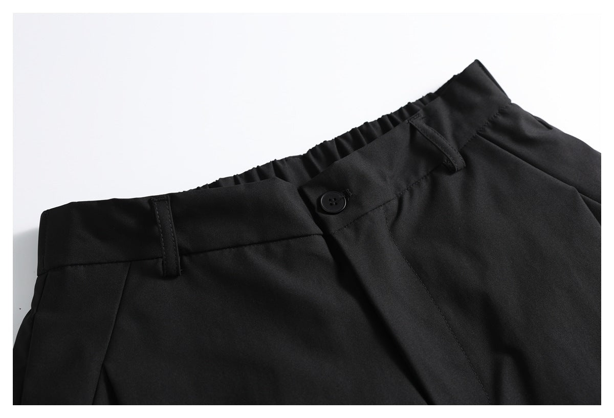 Close-up of black shorts showing the waistband, belt loops, button, and front pleat.
