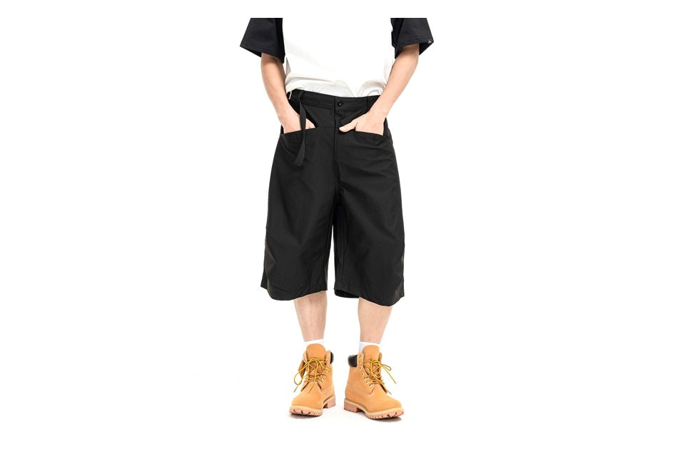 Front view of a model wearing loose black knee-length shorts with a white-and-black T-shirt.