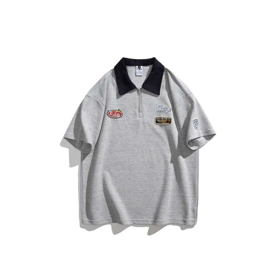 Heather gray waffle-knit short-sleeve polo with navy collar, quarter zipper and chest patches, flat front view