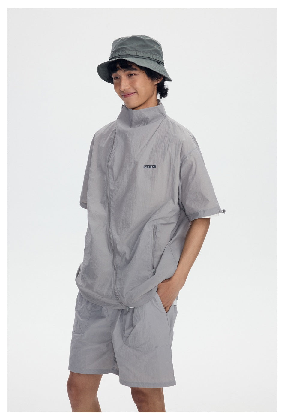 Model wearing a light gray short-sleeve zip jacket and matching shorts with a dark gray bucket hat.