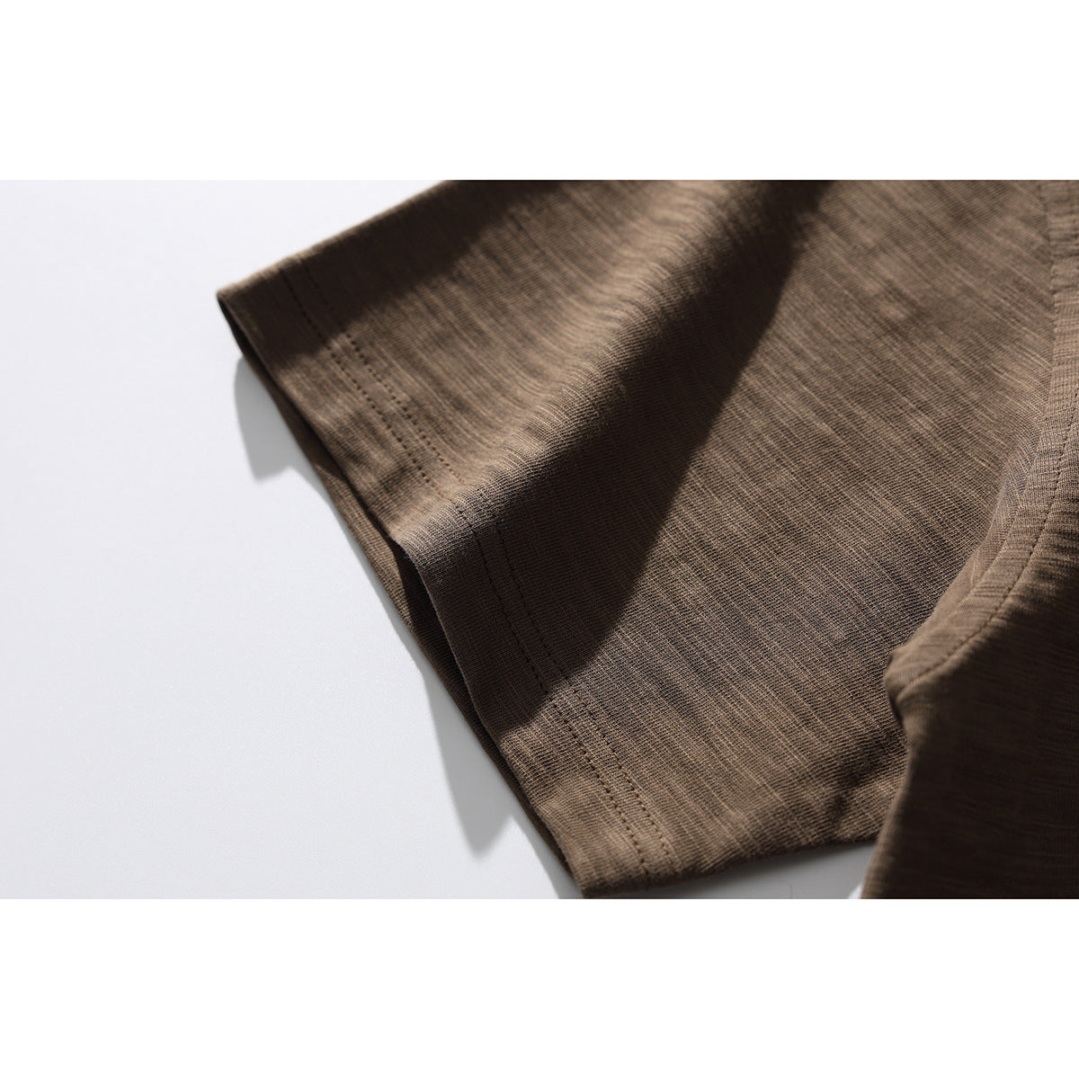 Close-up of the brown T-shirt sleeve hem and stitching on a white surface.