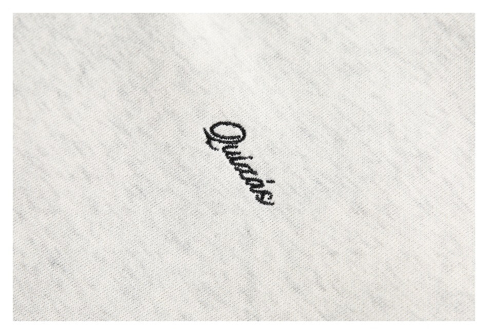 Close-up of a small black embroidered script logo on light heather-gray fabric.
