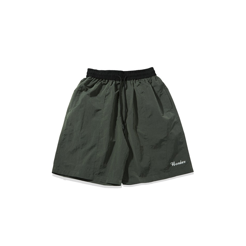 Dark olive green knee-length shorts with black waistband, drawstring and white script embroidery, flat lay