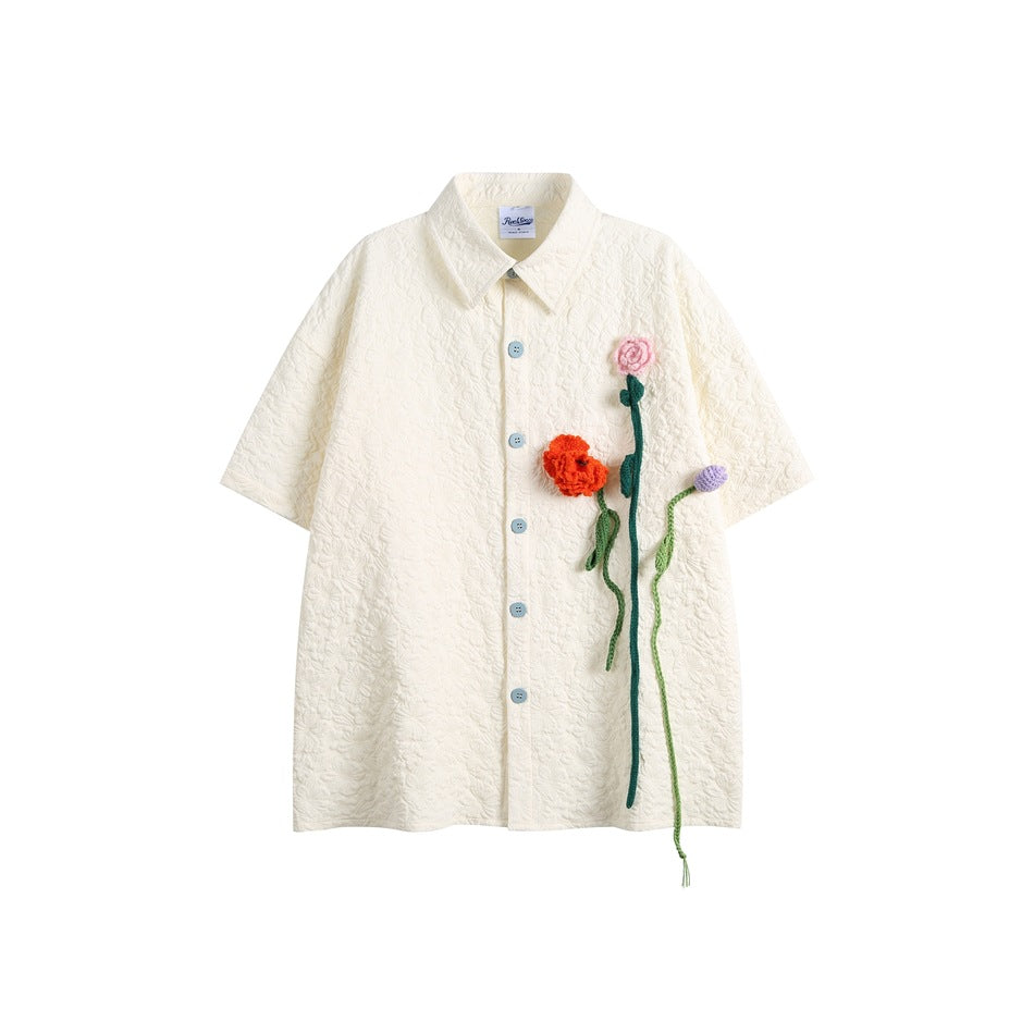 Off-white short-sleeve button shirt with raised floral texture, light blue buttons and crochet flowers on the chest