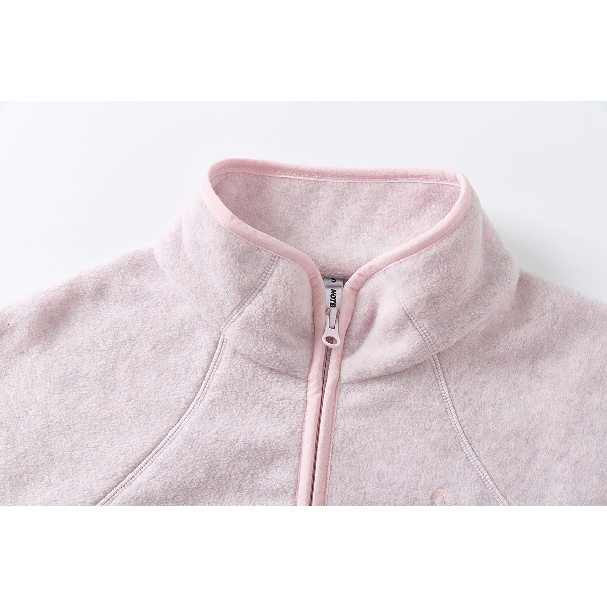 Close-up of a pale pink jacket's stand collar, front zipper, and curved seam details.