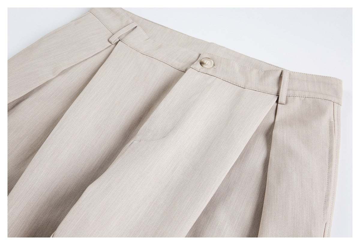 Close-up of beige trousers showing the waistband, button, belt loop, and front pleats.