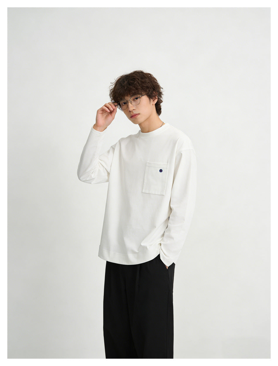 Model wearing a white long-sleeve crewneck top with a chest pocket, shown at an angle with black trousers.
