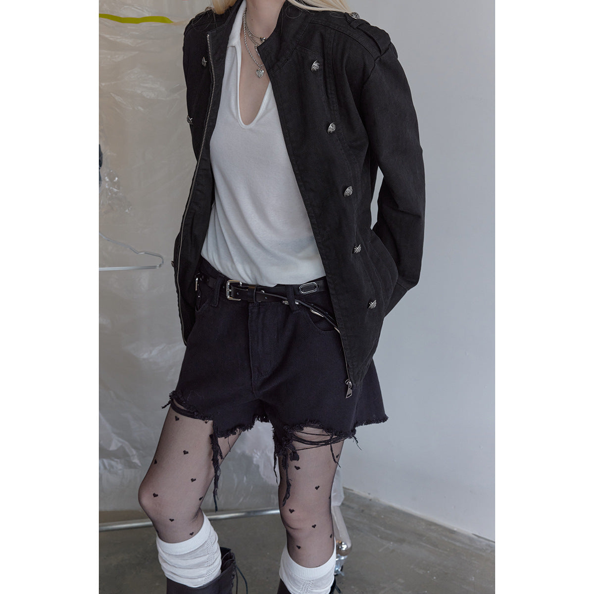 Cropped model view of a black buttoned jacket worn open with black shorts and patterned tights.