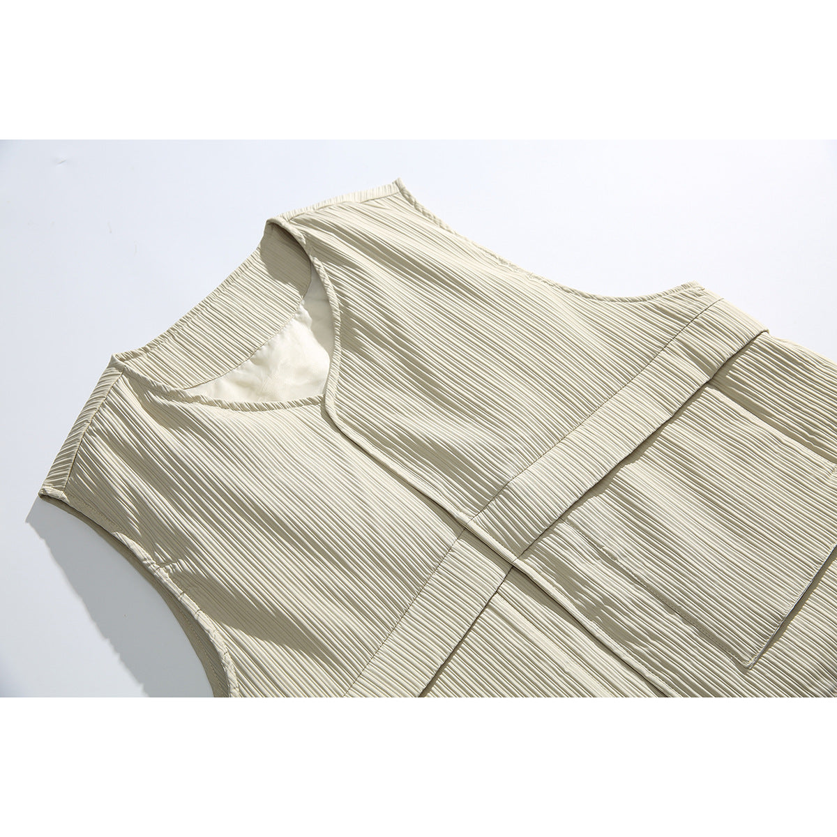 Close-up of an ivory sleeveless vest with a V-neck, pleated texture, and horizontal waist band.
