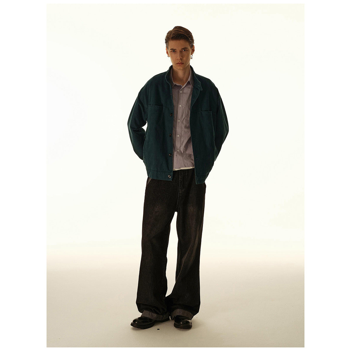 Full-length model wearing a dark teal button-front jacket over a muted mauve shirt and loose black trousers.