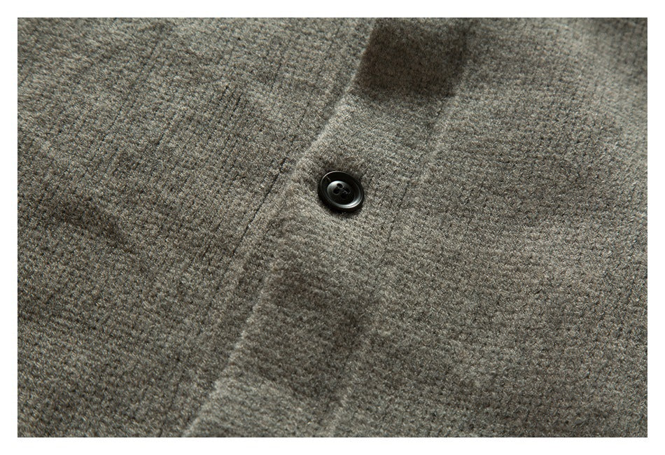Close-up of a dark button on the placket of a textured taupe-gray knit garment.