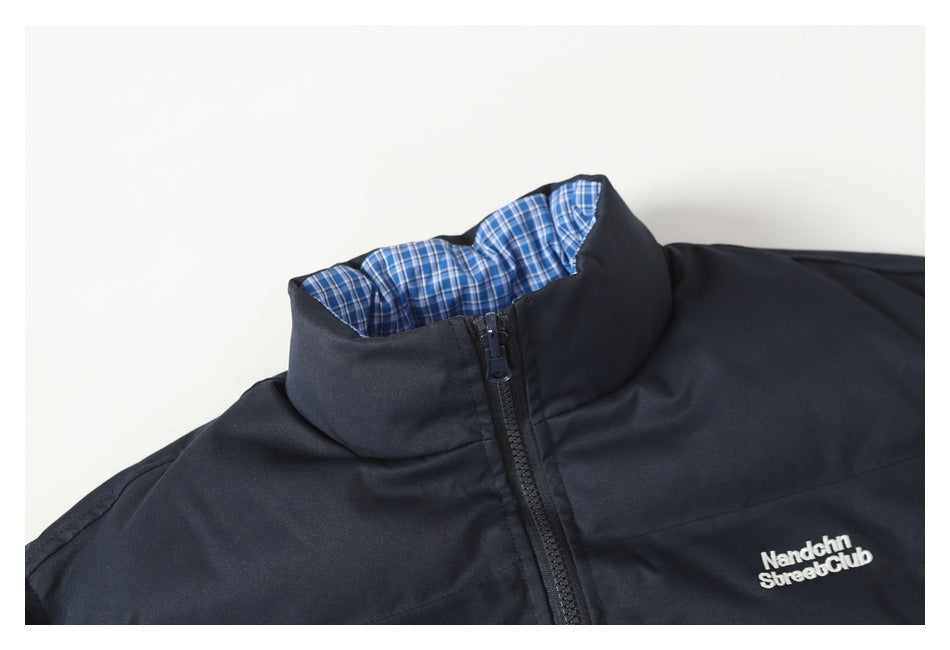 Close-up of a dark navy jacket collar with blue plaid lining, front zipper, and white chest embroidery.