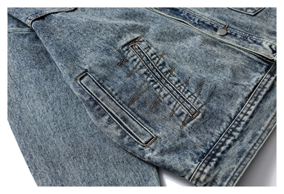 Close-up of decorative brown zigzag stitching beside a welt pocket on a blue acid-wash denim jacket.
