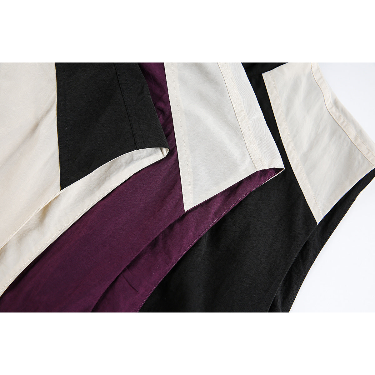 Close-up of overlapping cream, plum, and black vest hems with contrasting panels and stitched edges.