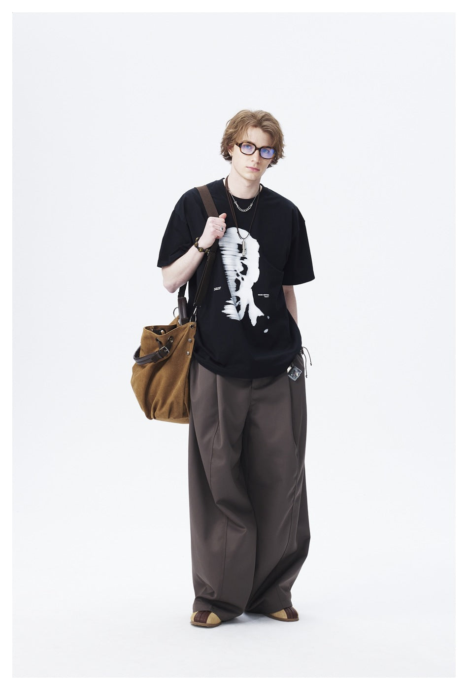 Full-length model wearing a black T-shirt with a large white abstract face graphic and loose dark trousers.