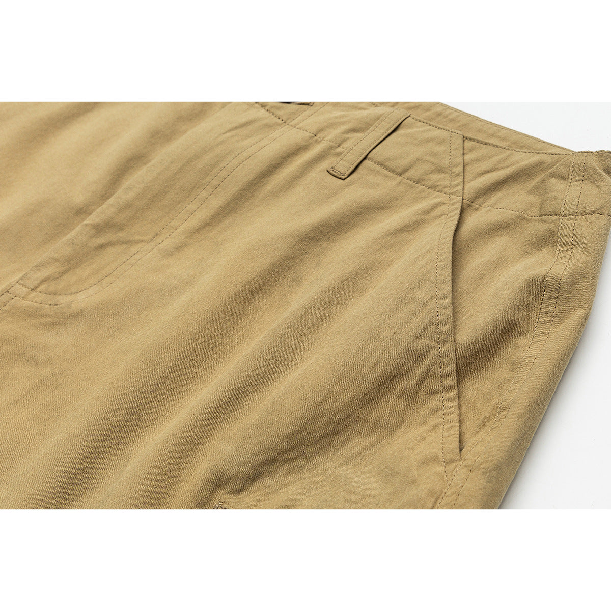 Close-up of tan shorts showing a belt loop, side seam and angled pocket opening.