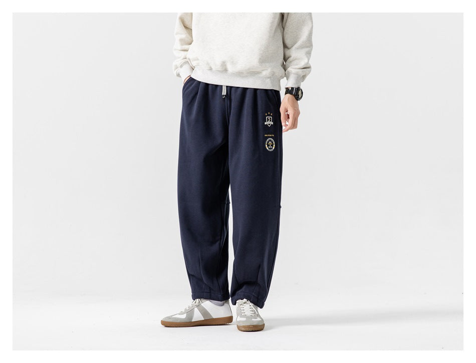 Front view of a model wearing navy relaxed joggers with a drawstring waist and embroidered thigh patches.