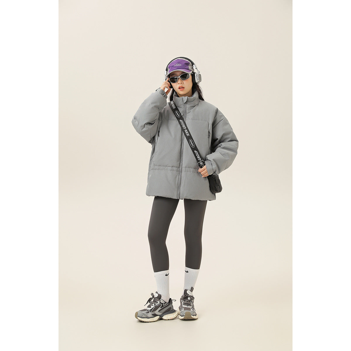 Full-length view of a model wearing a gray high-collar padded jacket with a front zipper and zip pockets.