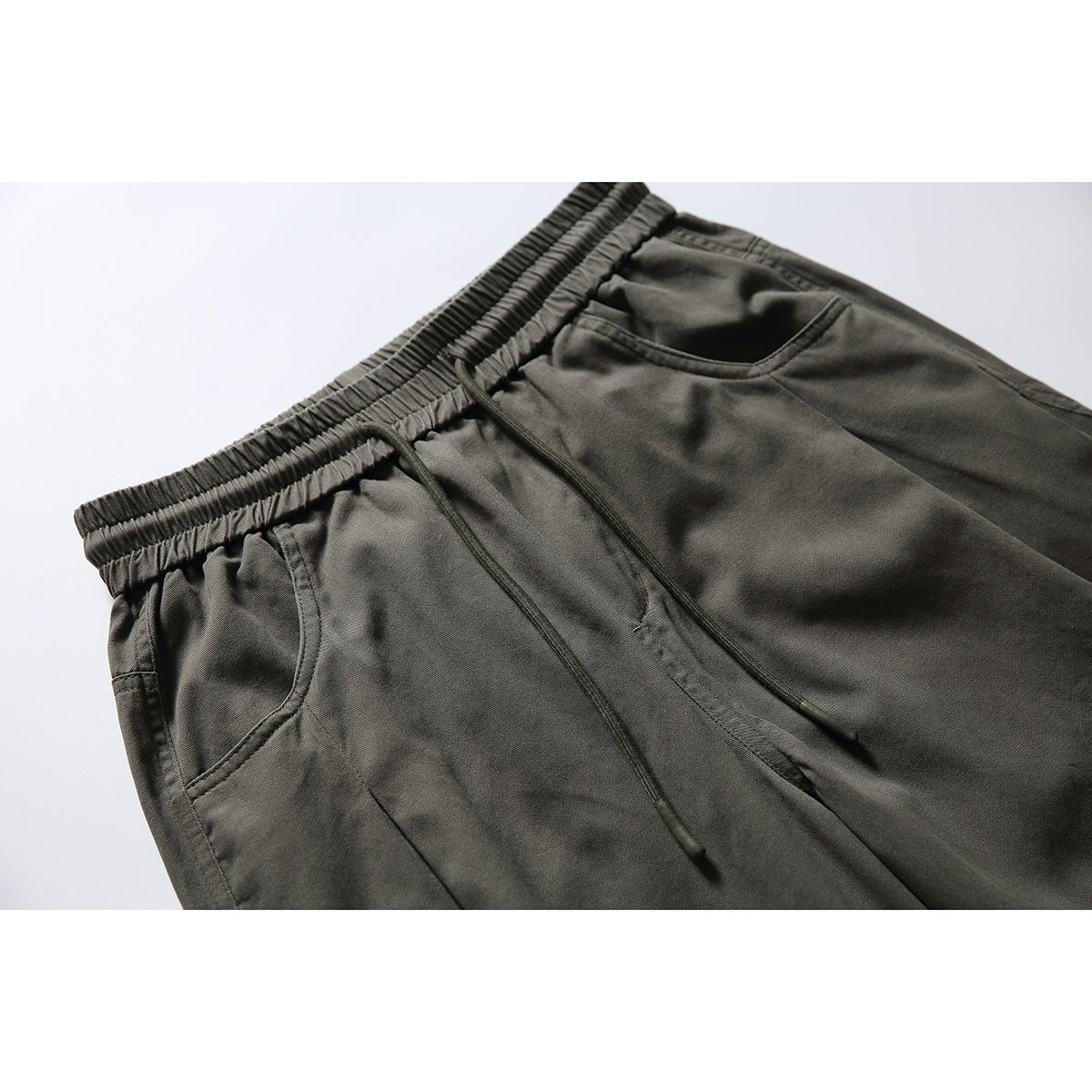 Close-up of dark olive pants showing the elastic drawstring waist and two front pockets.