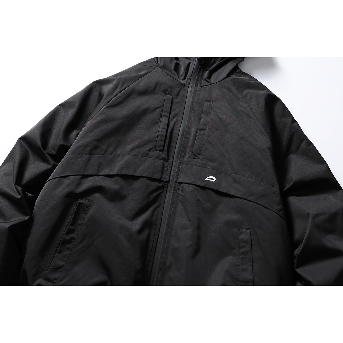 Close front view of a black hooded jacket with a center zipper, flap detail, pockets and a small white embroidered emblem.