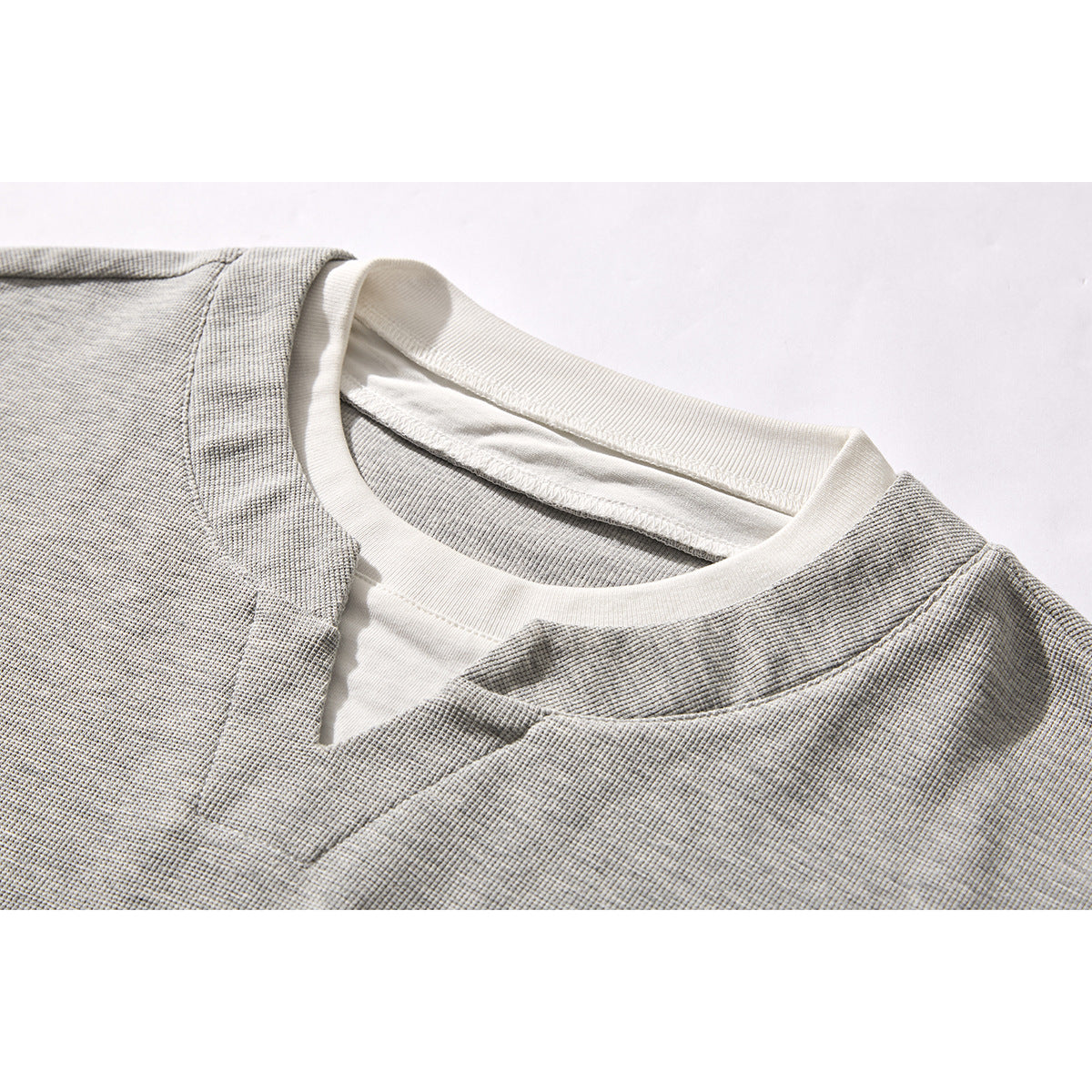 Close-up of a gray textured top's layered crew neckline with a white inner collar and small V-shaped notch.