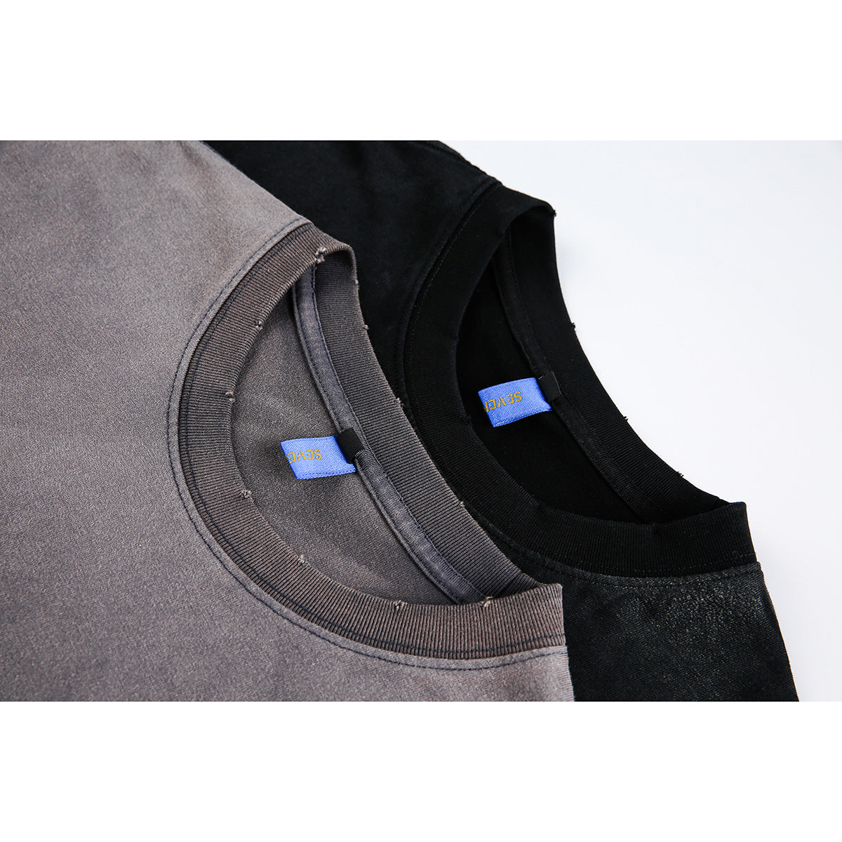 Close-up of ribbed crew necklines and blue labels on charcoal gray and black T-shirts.