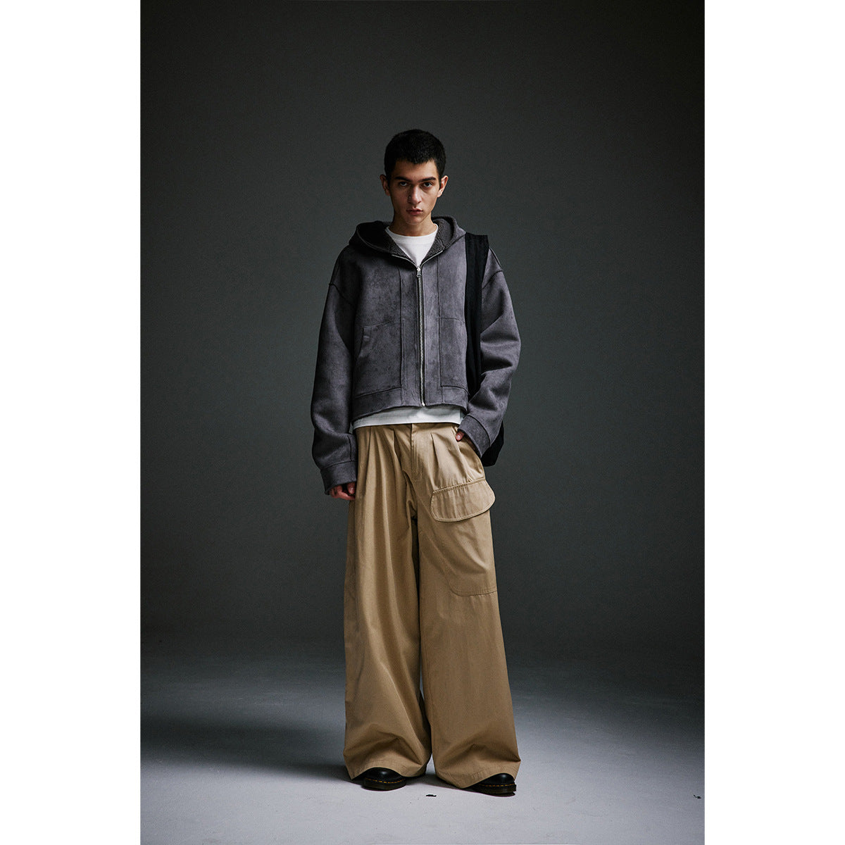 Front view of a model wearing a charcoal zip-up hoodie and very wide taupe cargo trousers.
