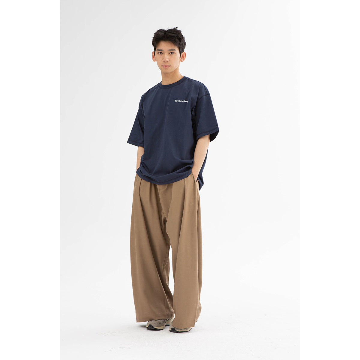 Model wearing a navy oversized T-shirt with small white chest lettering and loose tan trousers.