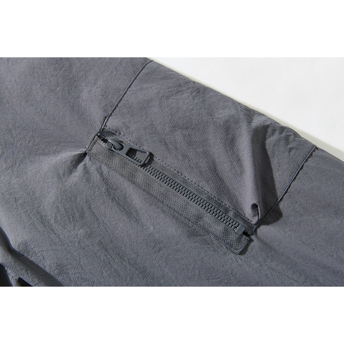 Close-up of a gray jacket’s angled zip pocket and zipper pull.