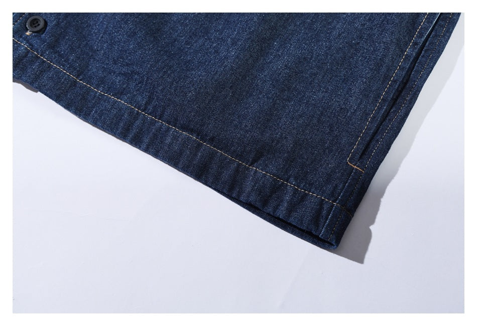 Close-up of a dark indigo denim garment hem, tan stitching, and a small black button.