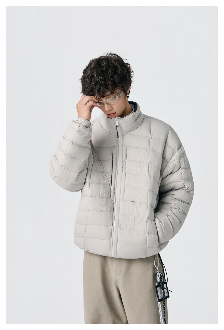 Model wearing a light gray quilted zip jacket with a high collar and beige trousers.